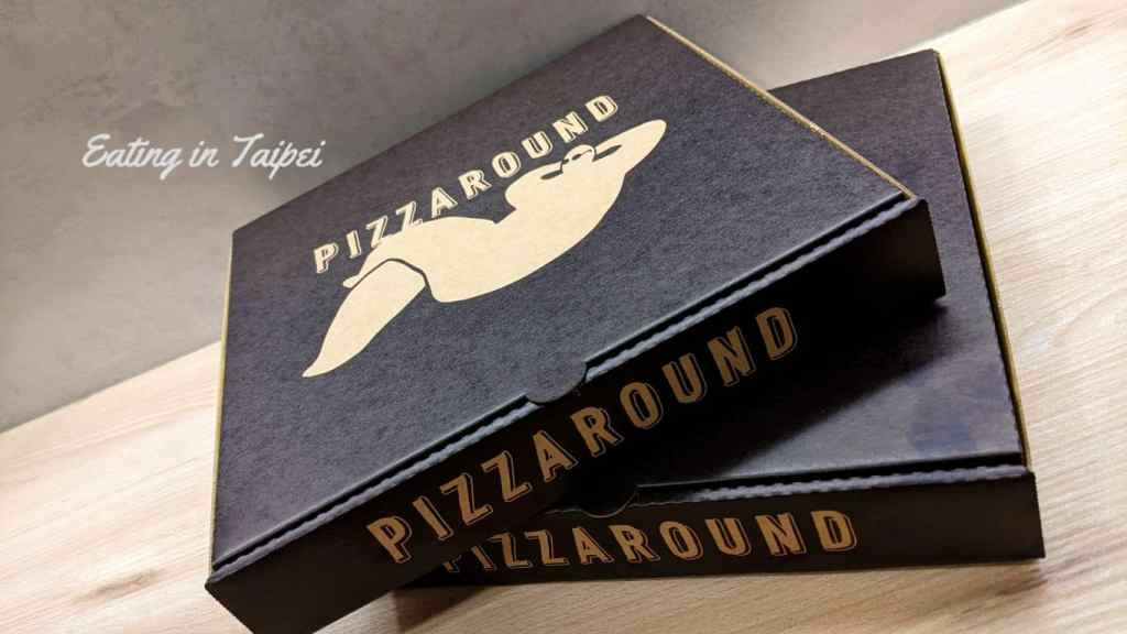 Pizzaround pizza boxes are modestly decorated, with Pizzaround written on the box above an unrecognizable person lying down and relaxing.